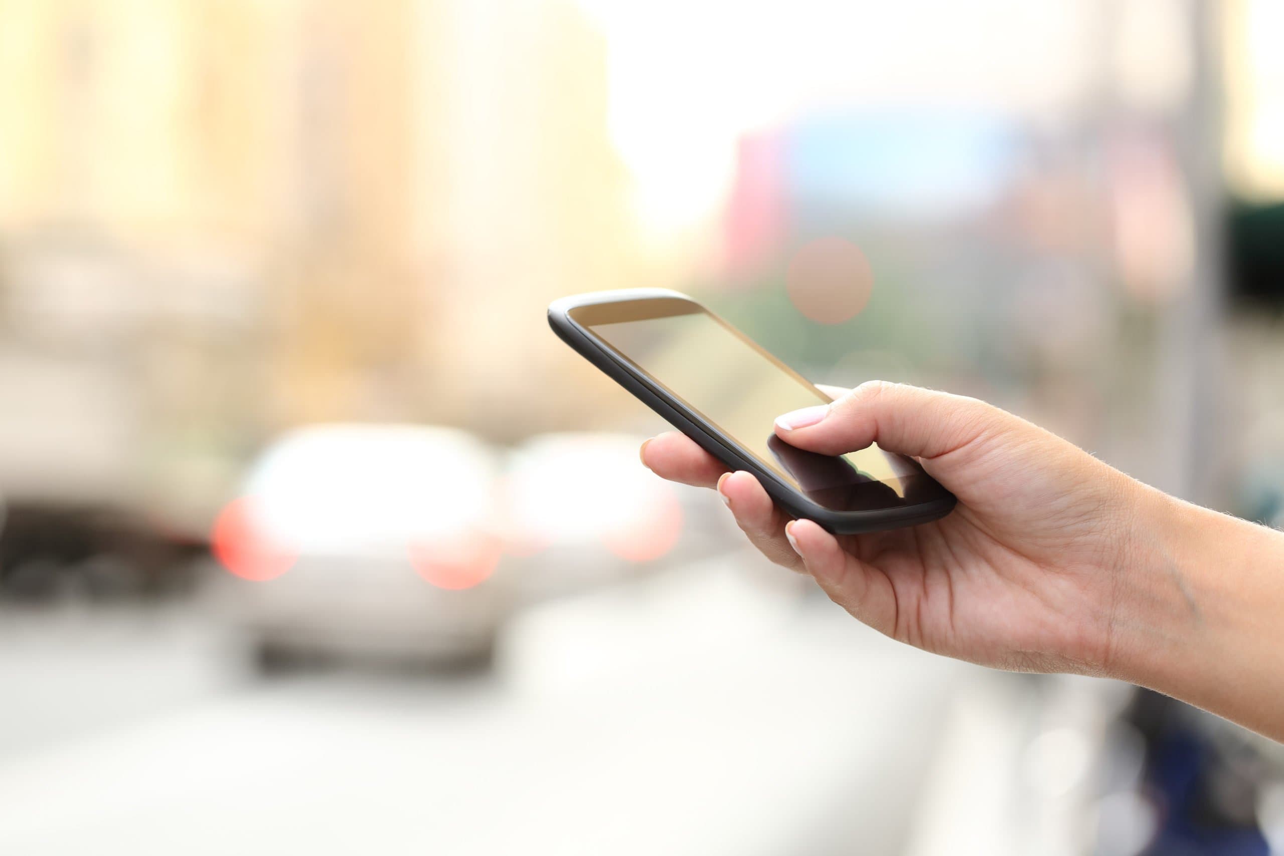 photodune-14387893-woman-hand-texting-on-a-smart-phone-in-the-street-xl-scaled
